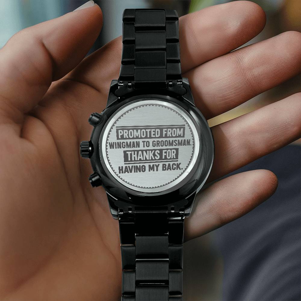 Black metal watch held in a hand with Promoted From Wingman to Groomsman Thanks For Having My Back engraved on the back.